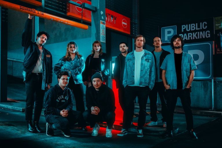 Indie band King of Spain posing together in a moody, neon-lit parking garage with red and blue lighting.